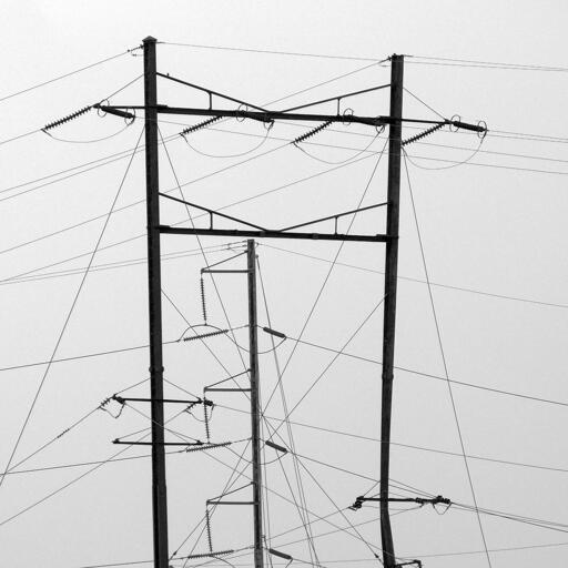 Abstract photo of railroad catenary pylons and wires against an indistinct grey sky.