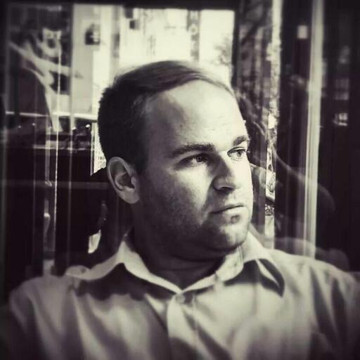 Black and white portrait of a man (me) sitting by a window with a thoughtful expression. The photo was taken in Paris in 2014, with soft lighting highlighting his facial features and a blurred background effect.