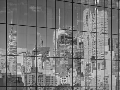 Abstract photo of the side of a glass curtain office building, with a grid formed by window sections, showing a distorted reflection of a crowded skyline of skyscrapers.