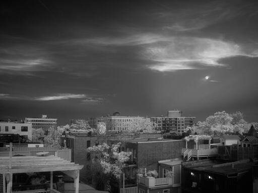 Clouds and a moon against a dark sky, over urban rooftops.