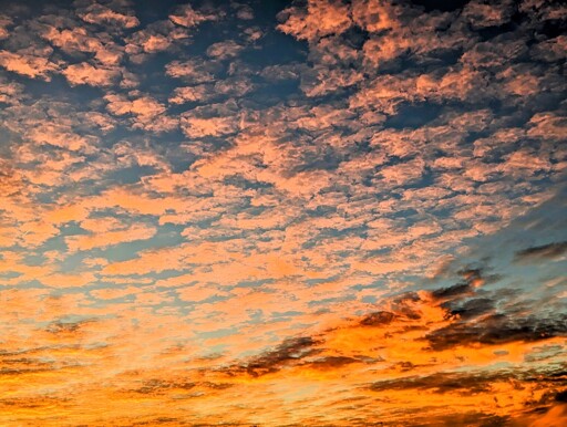 An orange sky at sunset. There are some clouds, reflecting the light. Everything is peaceful, silent and calm.