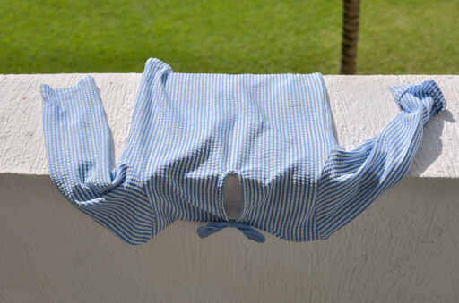 A color photo of a baby's swimsuit drying on a balcony in the sun. 