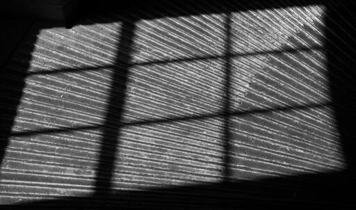 Abstract photo of the shadow cast by a window frame onto a corrugated metal floor.